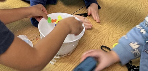 Children placing pom poms on the bowl.