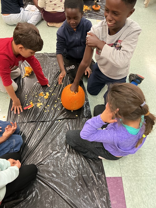 Group of children observing a peer put their hand inside a pumpkin