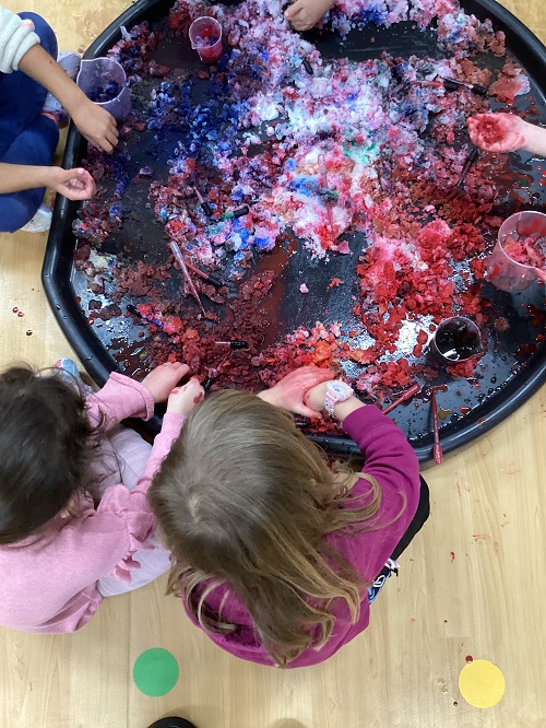 A group of children exploring with coloured snow in a tuff tray.