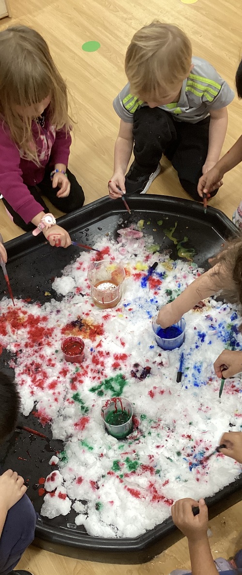 Children using water droppers to add colour to fresh white snow.