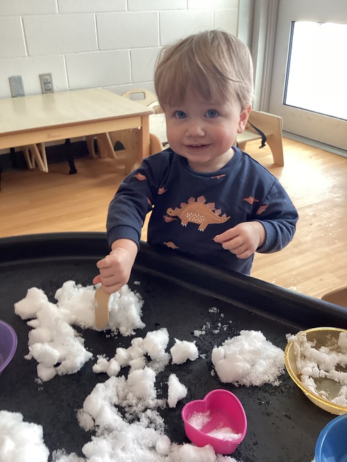 An infant child playing with snow in the tuff tray
