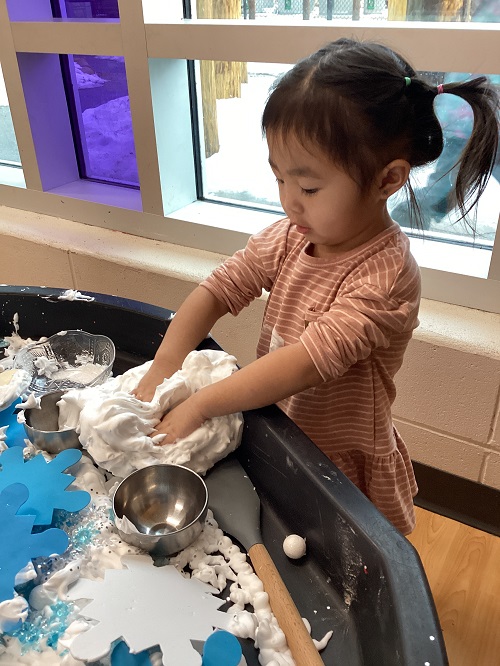 A preschool child using both hand to squish the shaving cream