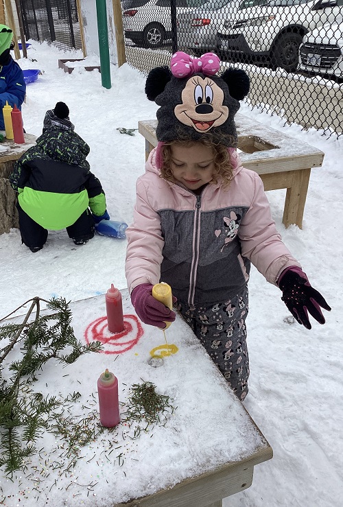 A child exploring with coloured water on the white snow.