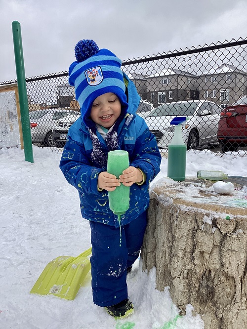 A child squeezing coloured water onto the white snow.