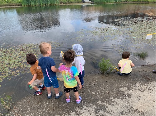 A group of children observing a pond in front of them.