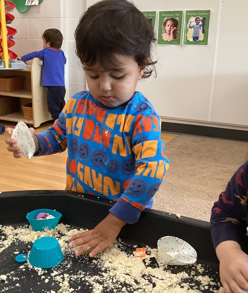 a toddler using their hand to squish an oil and flour mixture 