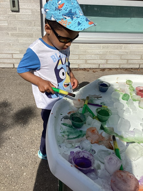 A toddler painting ice cubes on the tuff tray