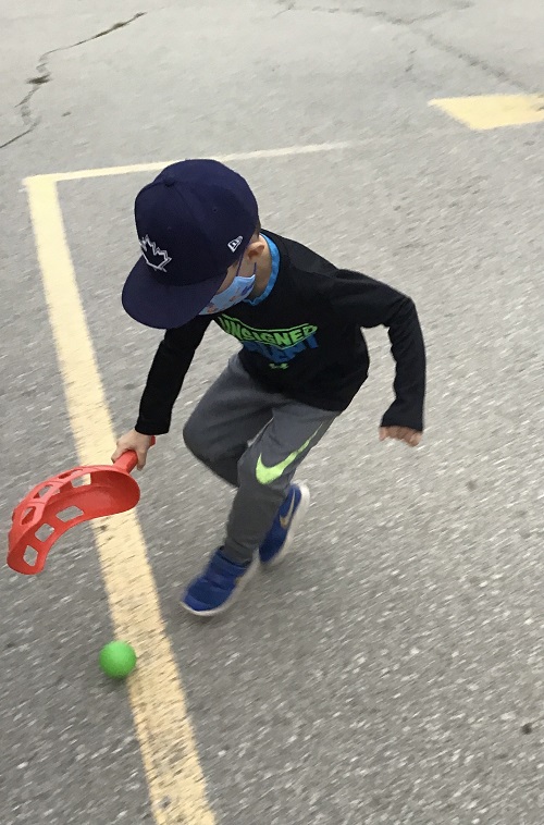 School age child in a hat chasing a small green ball with a red scope outside on ashphalt 