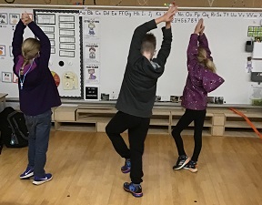 threes school age children standing on one leg with their arms over head 