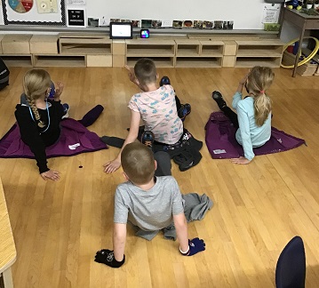 four school age children sitting on the floor moving thier elbow across their bodies to touch the opposit knee. 