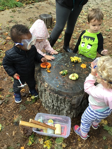 group of toddler children outside with googles on using hammers to smach small gourds
