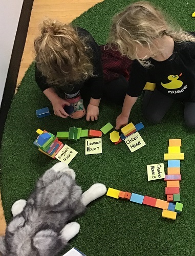 Two preschool children working with coloured, flat wooden blocks building housed for the three little pigs. 