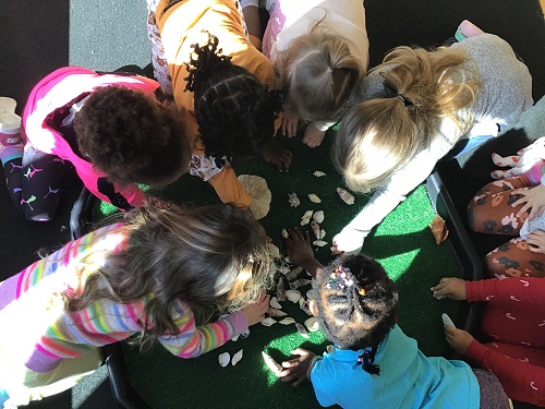 group of preschool children gathered over and black tuff tray with an assortment of loose materials