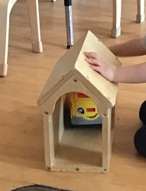 Child's hands visibly pushing  a toy care through a barn 