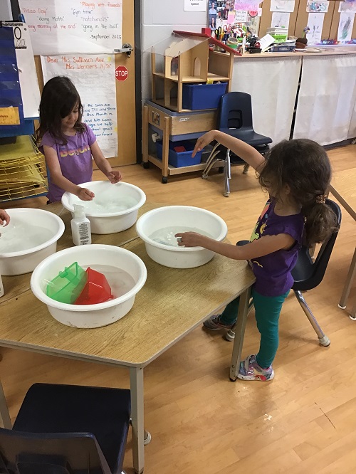 2 children sitting at a table with 4 white buckets each one with colored water
