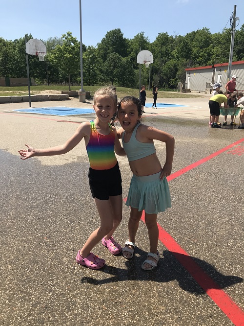 2 school age girls standing side by side outside on paved area