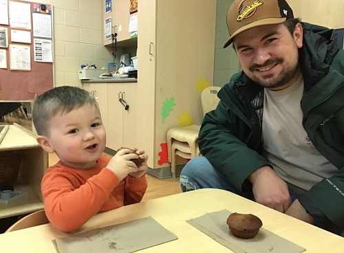 A child sitting with his father eating muffins together